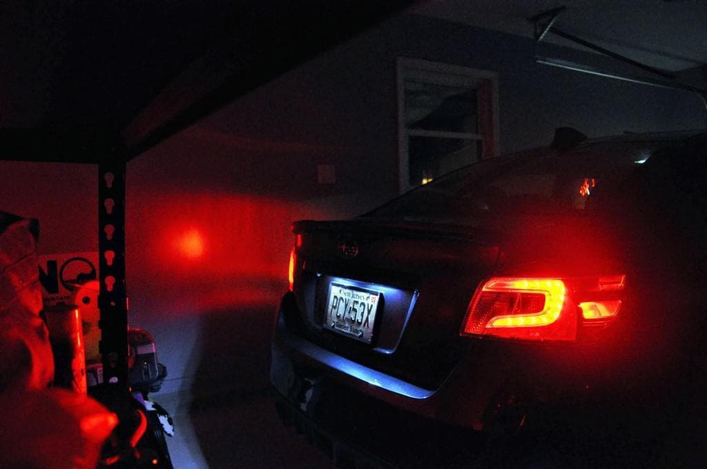 The rear of a dark saloon car in a garage at night, its plate lit white between red tail lights